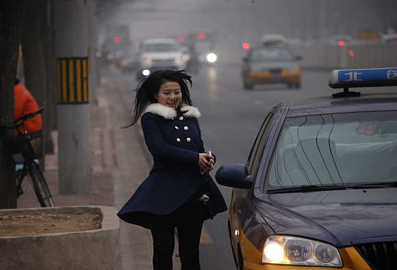A woman smiles as she runs to a taxi on a hazy day of Beijing.