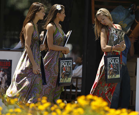 Women walk with polo magazines at the Campo Argentino de Polo in the Buenos Aires.