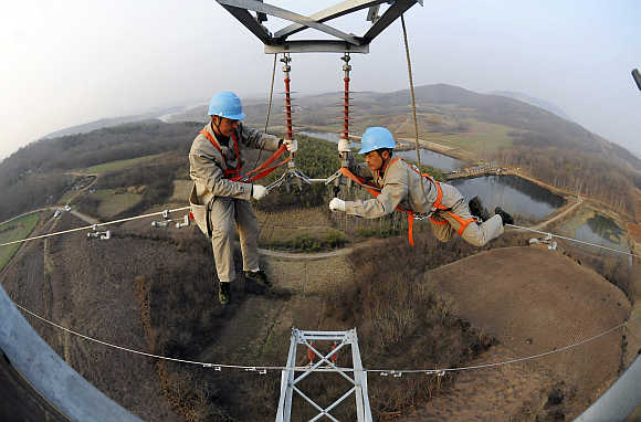 Workers check on electricity pylon situated amid farmlands in Chuzhou, Anhui province, China.