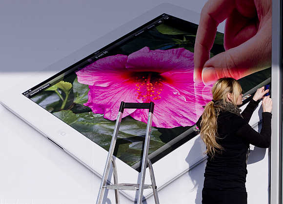 A woman pastes an advertising poster showing Apple's iPad tablet computer to the window of an electronic retailer in Berlin, Germany.
