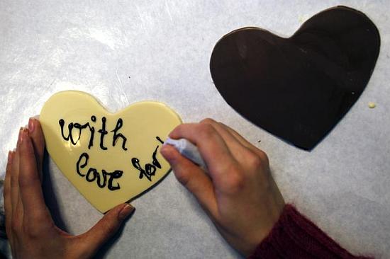 A woman writes a love message on a small chocolate heart.