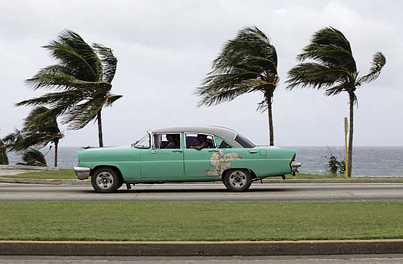 People ride a taxi as strong winds blow palm trees in Havana.