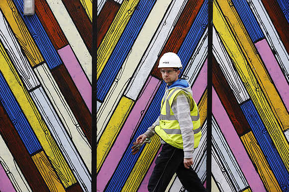 A construction worker walks past a colourful hoarding in the city of London.