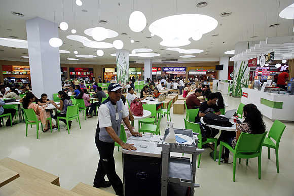 A cleaner pushes a trolley as customers eat at the foodcourt of a shopping mall in Mumbai.