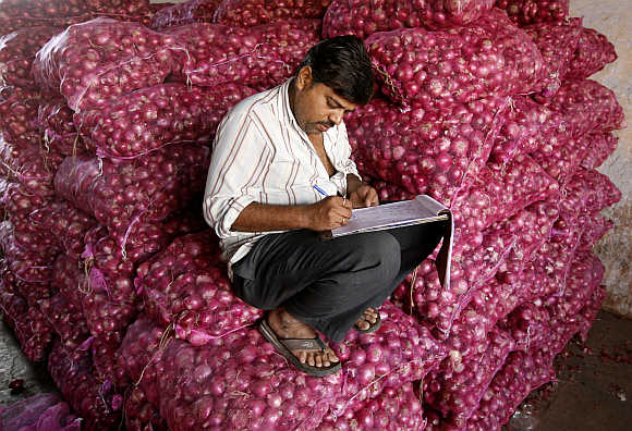 A trader works on his accounts while sitting on sacks of onions at a wholesale market in Ahmedabad.
