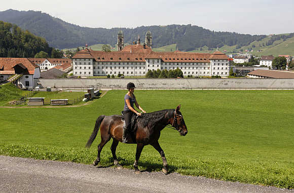 A woman rides a horse in front of Kloster Einsiedeln abbey in the central Swiss town of Einsiedeln.