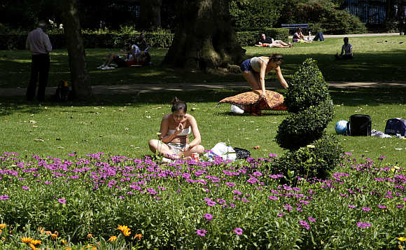 A woman reads a book in a garden on a sunny day in downtown London.