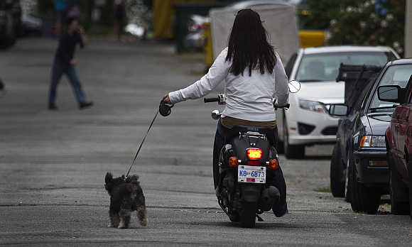A woman rides a scooter while taking her dog for a walk in downtown Vancouver, British Columbia.