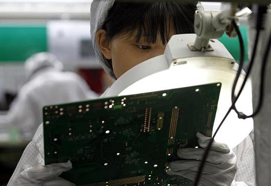 A worker examines a circuit board at an Apple's contract manufacturer. Apple chips are based on ARM's architecture.