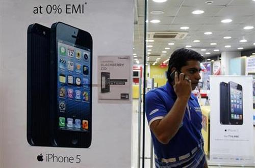 A man speaks on his mobile phone while standing next to posters advertising an Apple iPhone 5 and Blackberry Z10 in Ahmedabad.