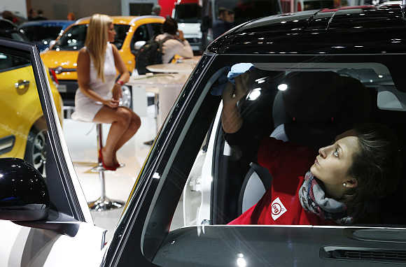 A worker cleans the windshield of a car next to a model during the European Motor Show in Brussels, Belgium.