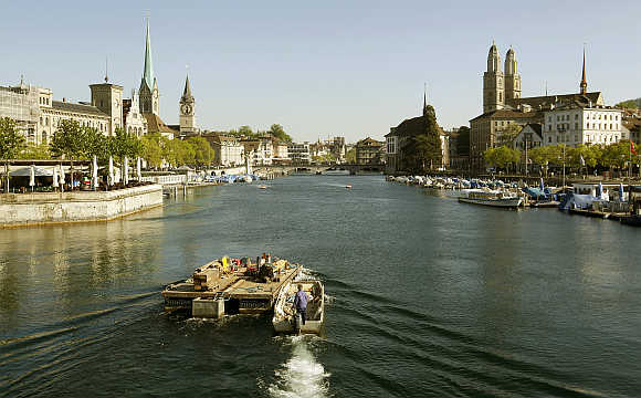 A man steers a boat and a pontoon on the Limmat River in Zurich.