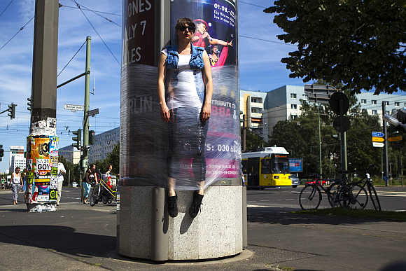 A woman is held to a rotating advertising column with cling film as a temporary installation of the Bosso Fataka street art group in Berlin.
