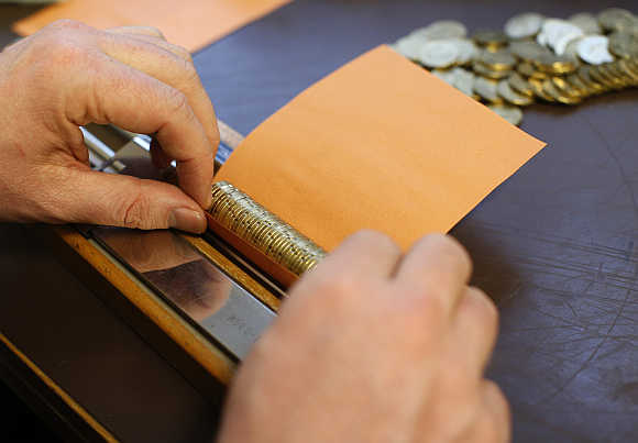 A bank employee rolls euro coins in paper in Gammesfeld, Baden-Wuerttemberg, Germany.