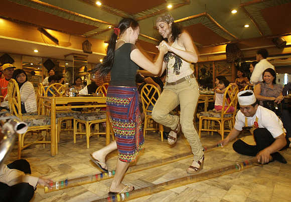 A waitress teaches a tourist how to dance the 'Tinikling', a native bamboo dance, in a Manila restaurant.