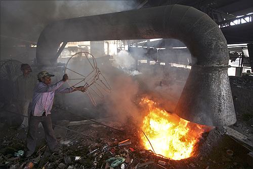 worker throws a broken iron chair into a furnace for recycling at an iron and steel factory on the outskirts of Jammu.