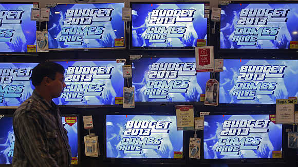 A man walks past television screens showing an advertisement for a programme on India's annual budget at an electronics shop in Mumbai.