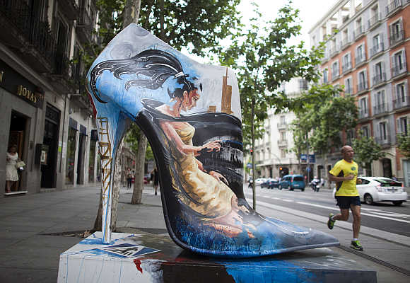A man jogs past a giant shoe figure, which is part of an exhibition entitled Shoe Street Art, in Madrid.