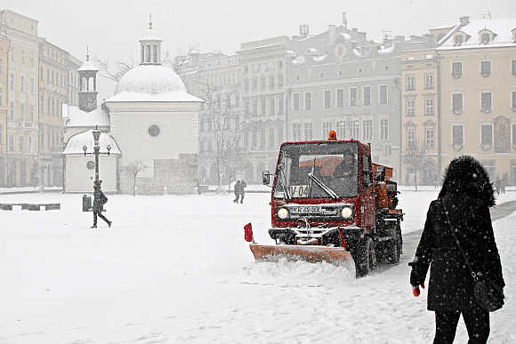 A woman walks as a snow-plough plows snow from the main market square after heavy snowfall in Krakow.