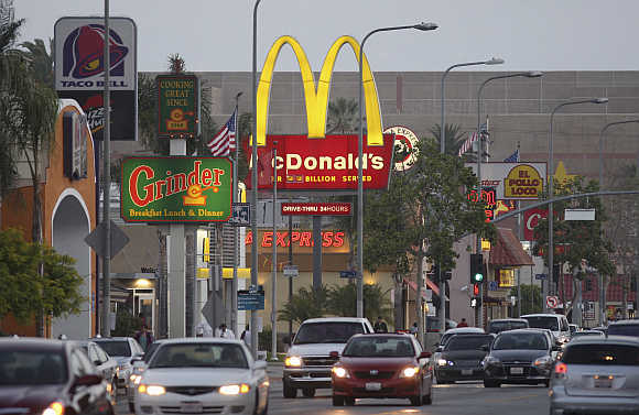Cars drive past the signs of restaurants along a busy street in Los Angeles.