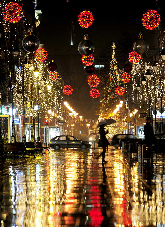 A woman walks near trees illuminated with Christmas lights in Skopje.