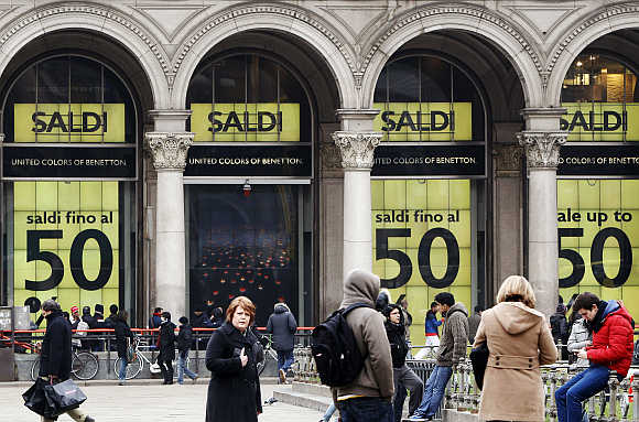 People walk in front of a department store having a sale in downtown Milan.