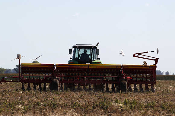 A worker drives a tractor pulling a sowing machine to plant soybeans in Estacion Islas, Buenos Aires, Argentina.