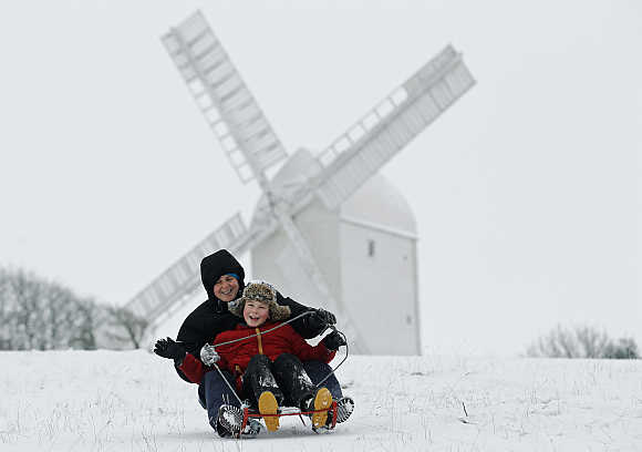 Eight-year-old Carl Attwater and his mother Jane ride a sled downhill in front of the Jill Windmill at Hassocks in England.