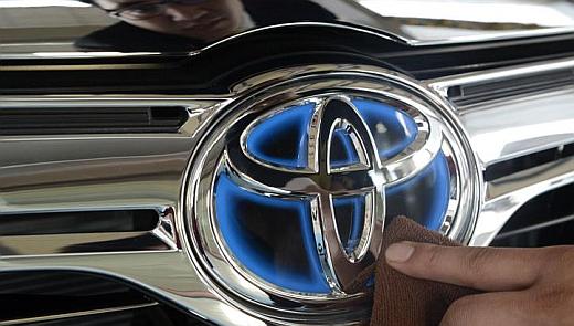 A worker cleans the logo of a Toyota car at dealership store.