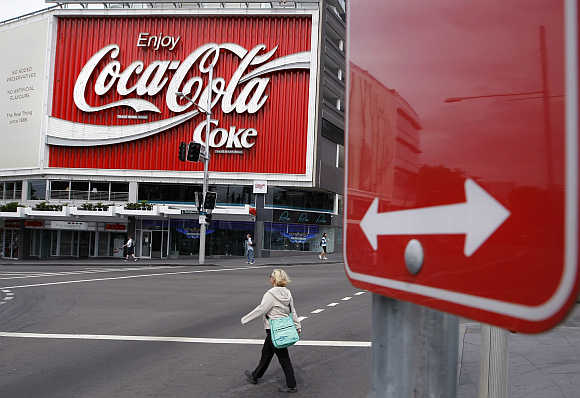 A pedestrian crosses a road in front of an outdoor Coca-Cola advertisement in Sydney.