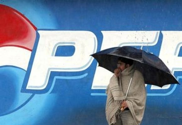 A man stands next to a Pepsi advertisement while using an umbrella in the rain