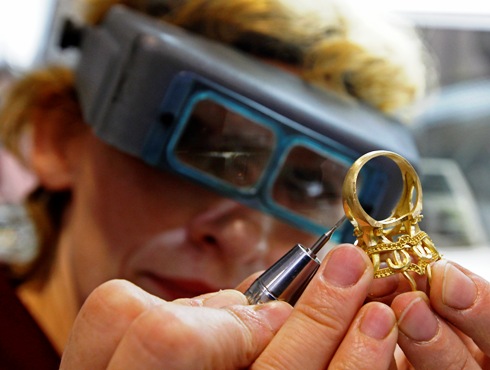 A jeweller works on a golden ring at a factory.