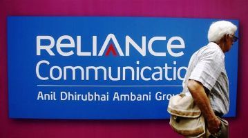 Image: A man walks past a logo of Reliance Communication before the Annual General Meeting in Mumbai.