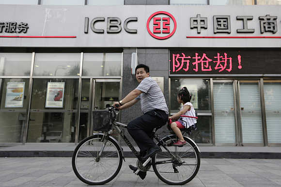 A man cycles a bike carrying his daughter past a branch of Industrial and Commercial Bank of China in Beijing.