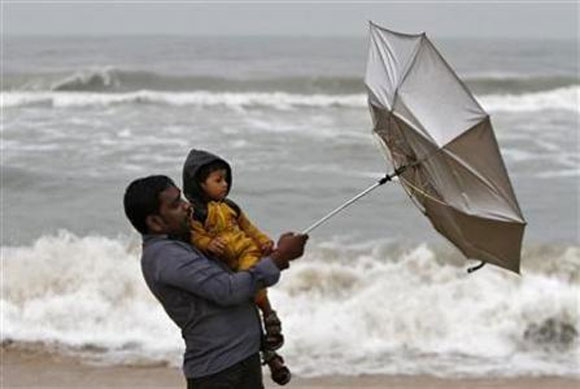 A man carrying his child tries to hold an umbrella at Marina beach in Chennai.