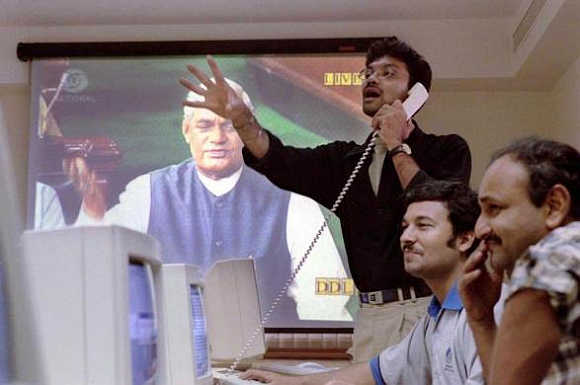 Stock brokers at a brokerage firm in Mumbai trade in front of a television screen displaying Atal Behari Vajpayee delivering his parliament address in New Delhi, April 17, 1999.