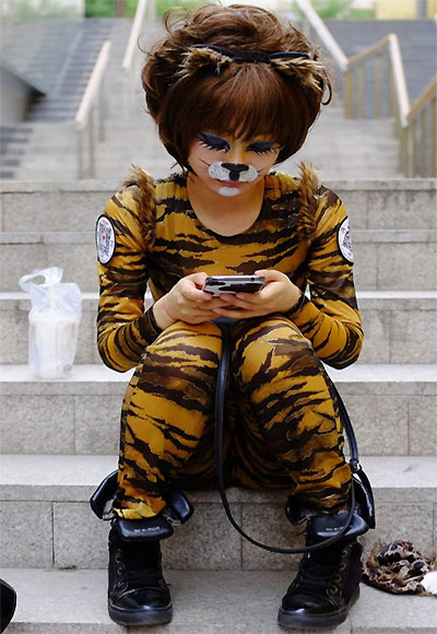 A volunteer wearing an animal costume checks her mobile phone as she waits to perform in an event promoting a love for dogs.