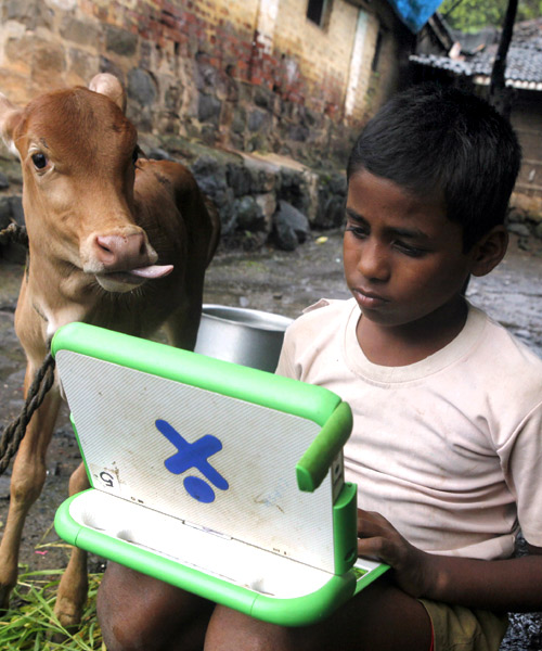 A schoolboy uses a laptop provided to him under 'one laptop per child' project by non-governmental organisation (NGO) as a calf stands near him at Khairat village, near Mumbai.