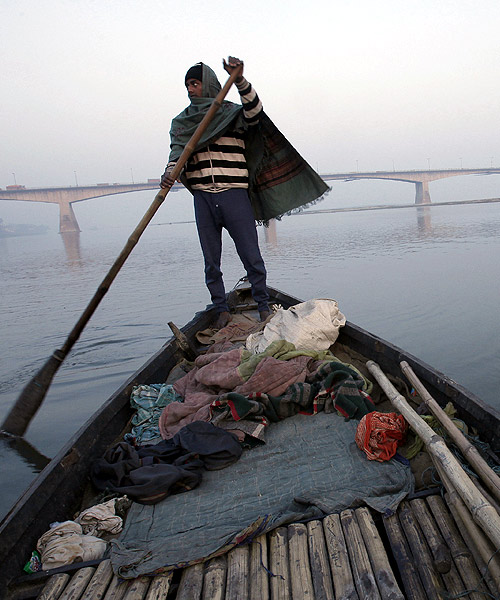 A man rows his boat in the waters of river Ganges with Mahatma Gandhi Setu bridge seen in the background in Patna.