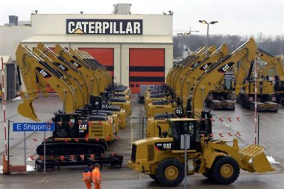 Workers walk past Caterpillar excavator machines at a factory in Gosselies.