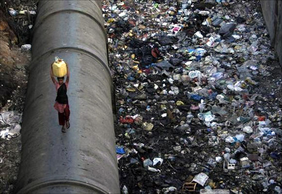 A girl carries water as she walks on a pipe in a polluted slum area in Mumbai.
