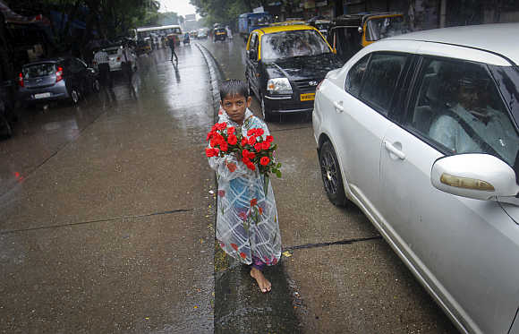 A boy sells roses while standing on a road divider during monsoon rains in Mumbai.