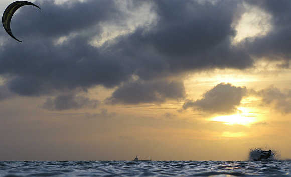 A kite surfer is silhouetted at the sunset while surfing a wave on his board in Aruba.