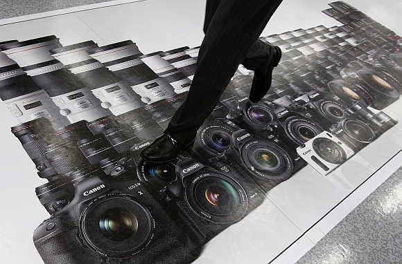 A man walks on an advertisement of Canon digital cameras at an electronics store in Tokyo. Canon is one of Dentsu's clients.