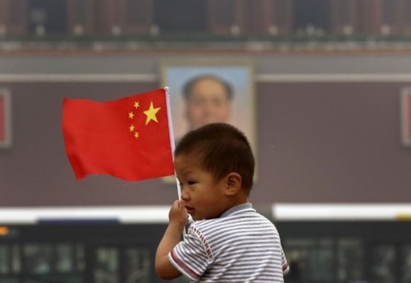 A child holds a Chinese national flag in front of a portrait of China's late Chairman Mao Zedong.
