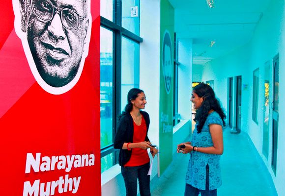Employees talk as they stand next to flex board poster of Infosys founder Narayana Murthy at the Start-up Village in Kochi.
