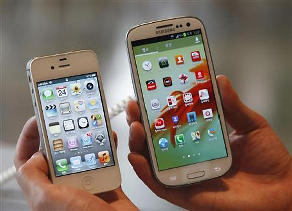 An employee poses as he holds Apple's iPhone 4s (L) and Samsung's Galaxy S III at a store in Seoul.