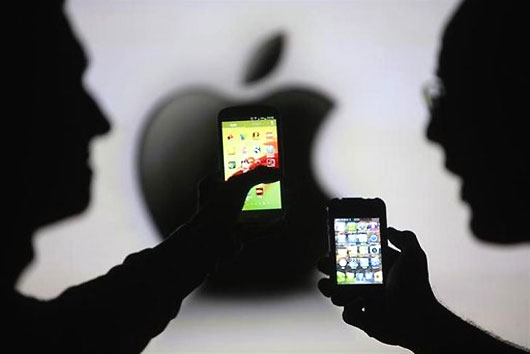 Men are silhouetted against a video screen as they pose with Samsung Galaxy S3 and iPhone 4 smartphones.