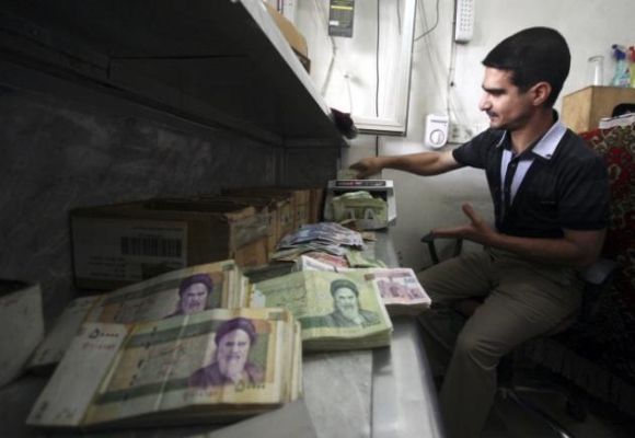 Man counts stacks of Iranian rials using a money-counting machine.