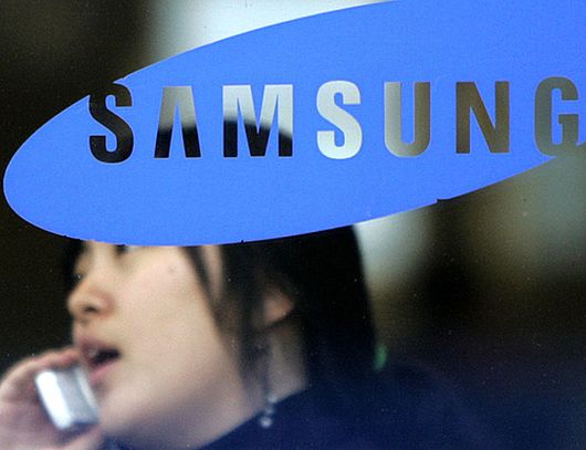 A woman uses her mobile phone behind a logo of Samsung Group in Seoul.